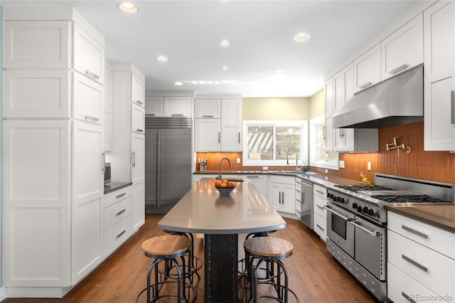 kitchen featuring white cabinets, premium appliances, recessed lighting, a breakfast bar, and under cabinet range hood