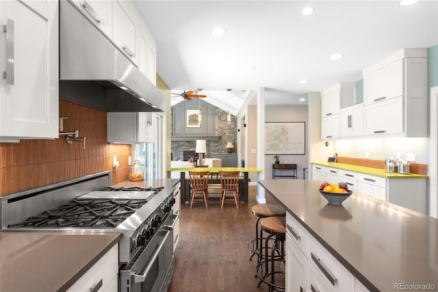 kitchen featuring tasteful backsplash, dark countertops, high end range, ceiling fan, and under cabinet range hood