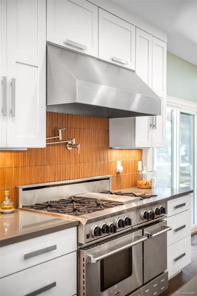 kitchen with decorative backsplash, range with two ovens, under cabinet range hood, and white cabinetry