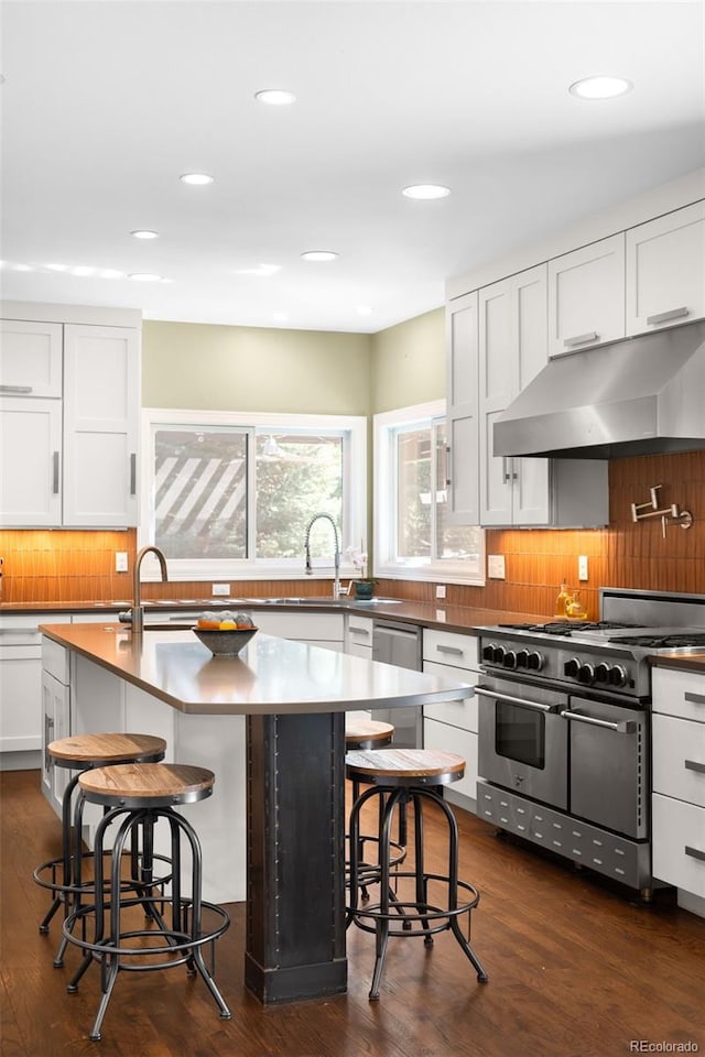 kitchen featuring under cabinet range hood, backsplash, appliances with stainless steel finishes, and a kitchen breakfast bar