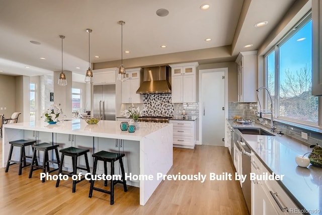 kitchen with built in refrigerator, wall chimney range hood, light wood-type flooring, and a kitchen bar