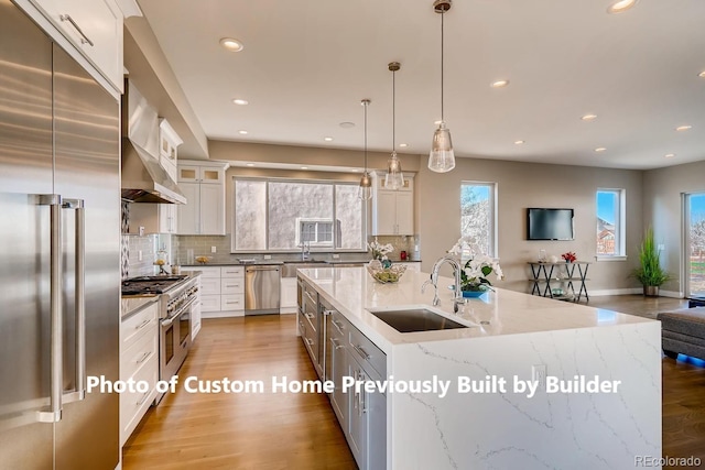 kitchen featuring wood finished floors, wall chimney range hood, premium appliances, and a sink