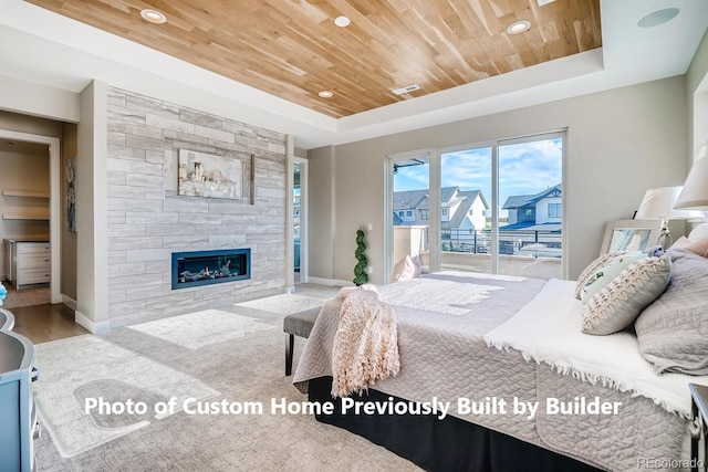 bedroom with access to exterior, a tray ceiling, wood ceiling, a stone fireplace, and baseboards