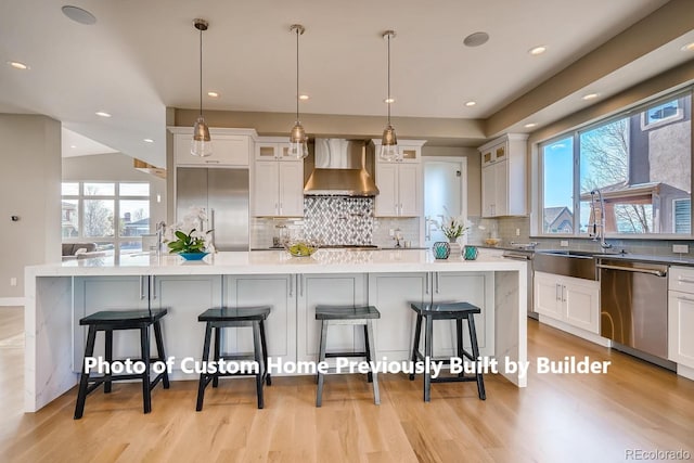 kitchen with a breakfast bar, stainless steel appliances, light wood-type flooring, wall chimney range hood, and a sink