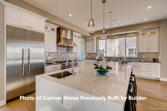 kitchen featuring wall chimney exhaust hood, white cabinetry, a sink, and built in refrigerator