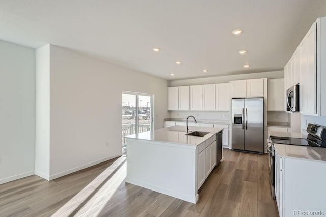 kitchen with stainless steel appliances, sink, white cabinets, and an island with sink