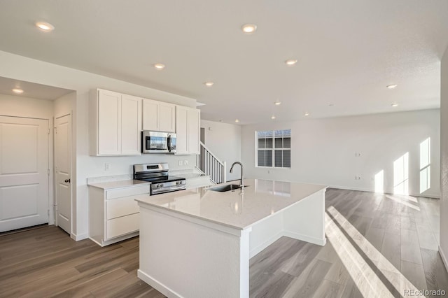 kitchen with white cabinets, stainless steel appliances, sink, a kitchen island with sink, and light wood-type flooring