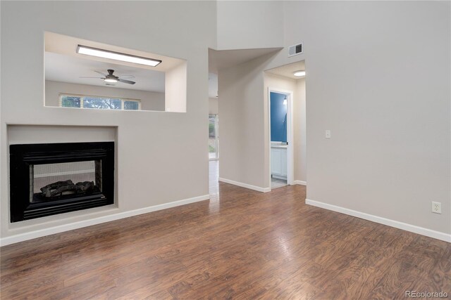 15828 Greenstone Ln, Parker, CO 80134 - unfurnished living room featuring a ceiling fan, wood finished floors, a multi sided fireplace, a high ceiling, and baseboards