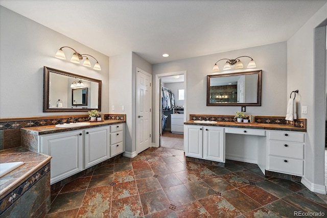 11691 Riverdale Dr, Parker, CO 80138 - full bathroom featuring stone tile flooring, two vanities, a walk in closet, a relaxing tiled tub, and recessed lighting