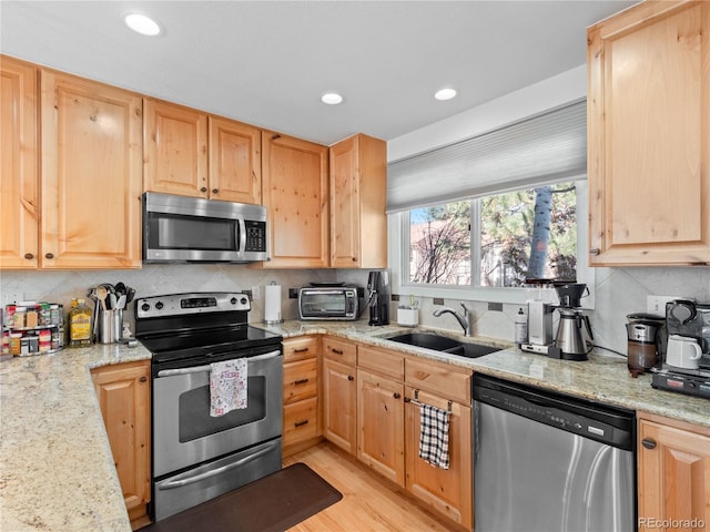 kitchen featuring tasteful backsplash, light stone counters, stainless steel appliances, light brown cabinetry, and a sink