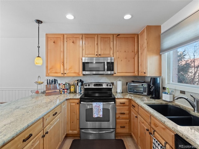 kitchen with a toaster, appliances with stainless steel finishes, light stone counters, and a sink