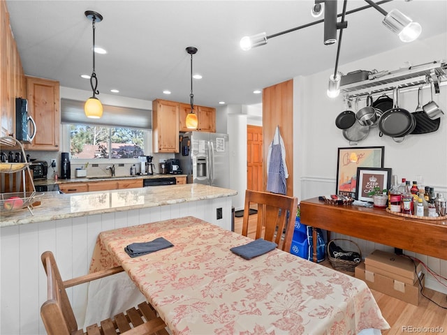 kitchen featuring decorative light fixtures, appliances with stainless steel finishes, light wood-style floors, a sink, and a peninsula