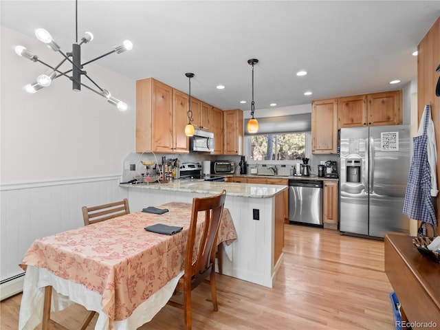 kitchen featuring hanging light fixtures, appliances with stainless steel finishes, light wood-style floors, a sink, and a peninsula