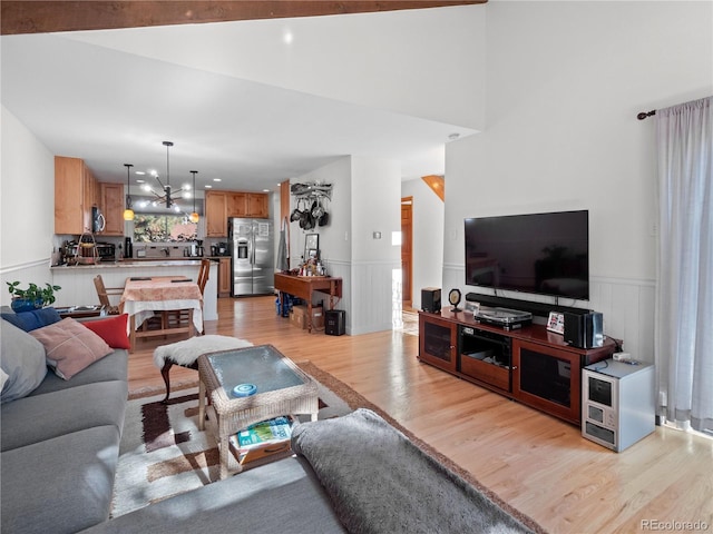 living area with light wood-style floors, a wainscoted wall, and an inviting chandelier