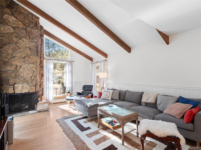 living room with vaulted ceiling with beams, a wainscoted wall, light wood-style flooring, and a stone fireplace