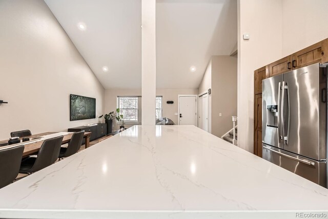 6443 S Florence Way, Englewood, CO 80111 - kitchen with stainless steel fridge, a spacious island, light stone counters, and high vaulted ceiling