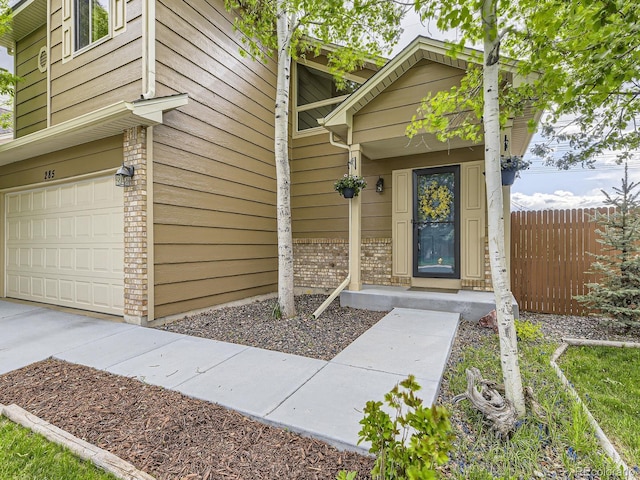 entrance to property with a garage, brick siding, and fence