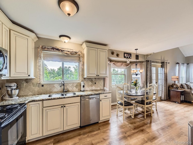 kitchen with stainless steel appliances, cream cabinetry, a sink, decorative backsplash, and light wood-style floors