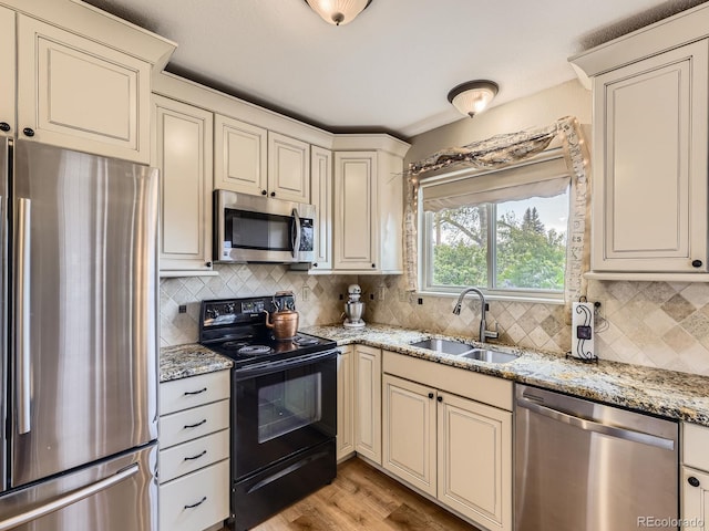 kitchen with stainless steel appliances, a sink, cream cabinets, tasteful backsplash, and light stone countertops