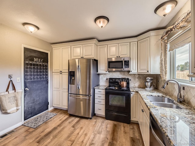kitchen with appliances with stainless steel finishes, a sink, tasteful backsplash, light wood finished floors, and light stone countertops