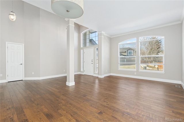 unfurnished living room featuring ornate columns, ornamental molding, a towering ceiling, and dark hardwood / wood-style flooring