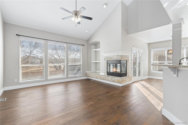 unfurnished living room featuring built in shelves, wood-type flooring, a multi sided fireplace, ceiling fan, and decorative columns