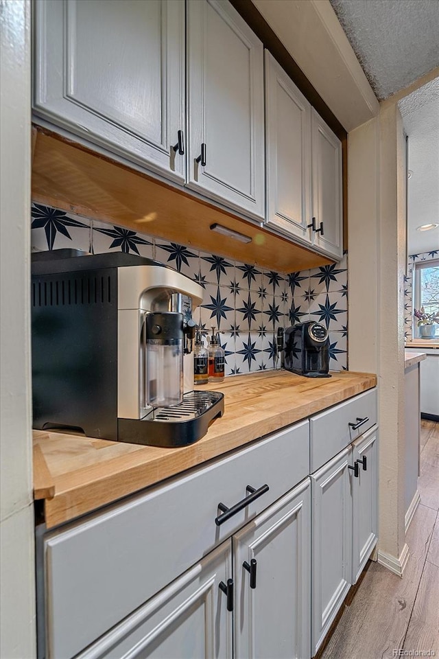 bar with butcher block countertops, decorative backsplash, a textured ceiling, and light wood-type flooring