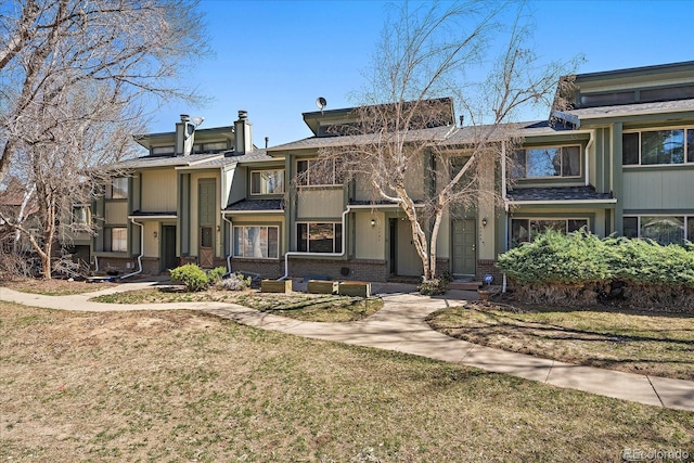 view of property with brick siding, a chimney, and a front yard