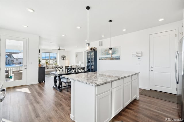 kitchen featuring a kitchen island, pendant lighting, white cabinets, light stone countertops, and dark wood-type flooring