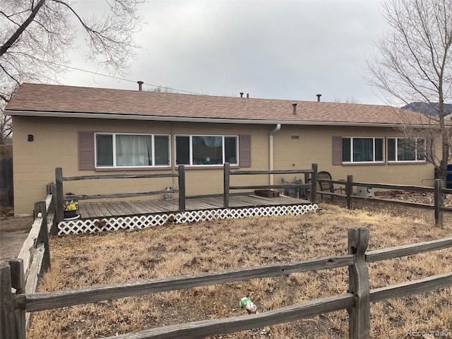 ranch-style house with fence, concrete block siding, a deck, and roof with shingles