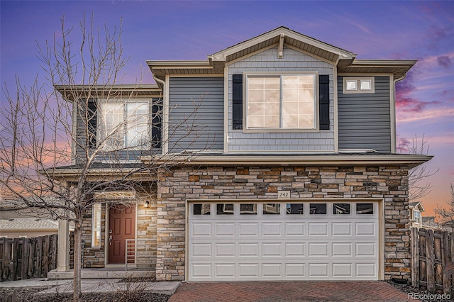 view of front of property featuring stone siding, decorative driveway, an attached garage, and fence