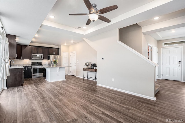 kitchen featuring appliances with stainless steel finishes, dark wood-type flooring, a tray ceiling, and a center island