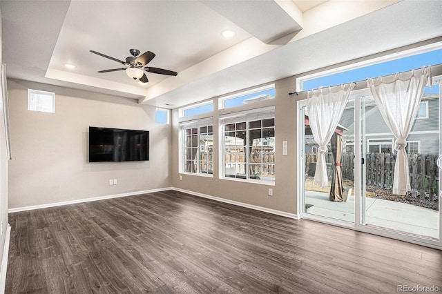 unfurnished living room featuring ceiling fan, baseboards, a tray ceiling, and dark wood finished floors