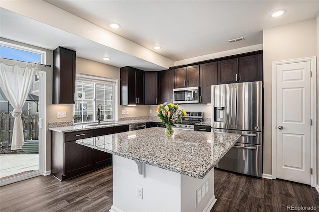 kitchen featuring dark wood-style floors, light stone counters, stainless steel appliances, dark brown cabinets, and a sink