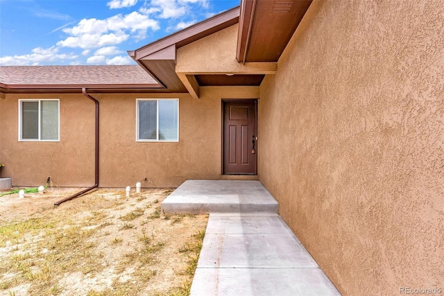 entrance to property with roof with shingles and stucco siding