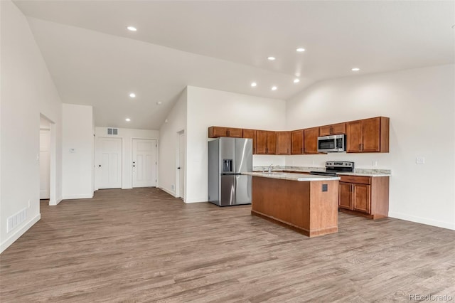 kitchen featuring appliances with stainless steel finishes, visible vents, light wood finished floors, and an island with sink