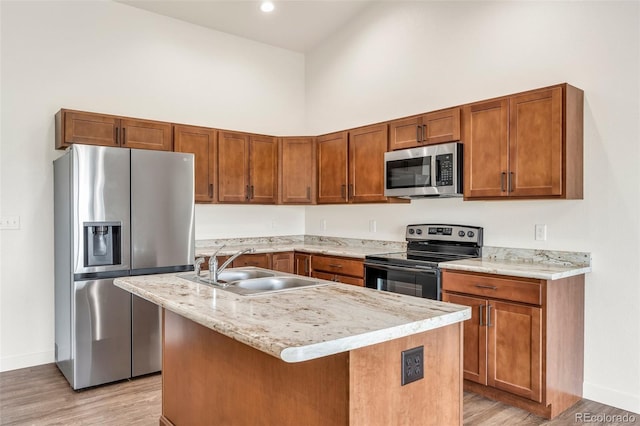 kitchen with a kitchen island with sink, a sink, a towering ceiling, appliances with stainless steel finishes, and light wood-type flooring