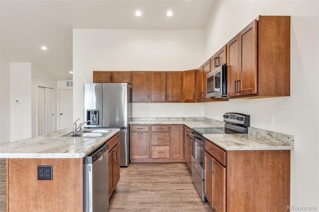 kitchen with light wood finished floors, appliances with stainless steel finishes, brown cabinets, and a sink