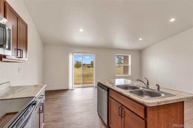 kitchen featuring a center island with sink, appliances with stainless steel finishes, wood finished floors, light countertops, and a sink