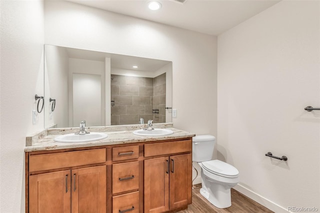 bathroom with tiled shower, a sink, toilet, and double vanity