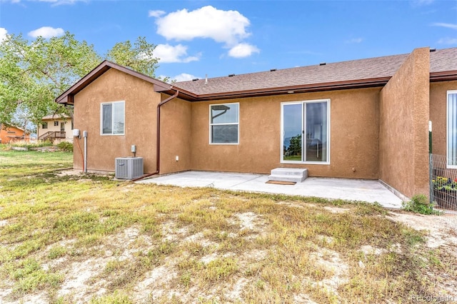 back of property with a patio, central AC, a shingled roof, a yard, and stucco siding