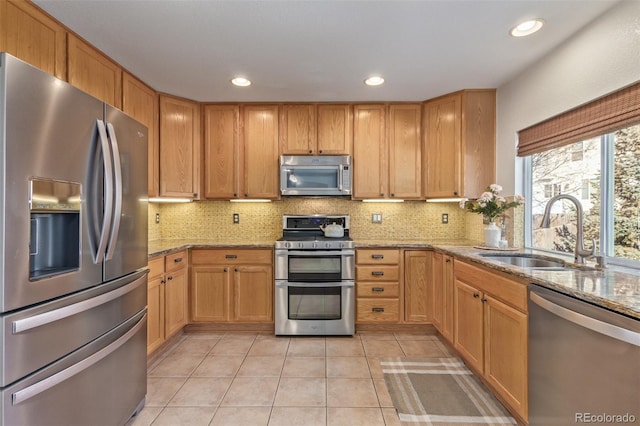 kitchen featuring stainless steel appliances, light stone countertops, sink, and decorative backsplash