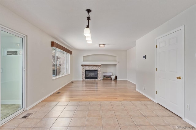 unfurnished living room featuring built in features, a tile fireplace, and light tile patterned flooring