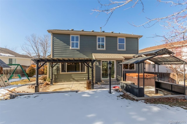 snow covered back of property featuring a patio area, a hot tub, and a playground