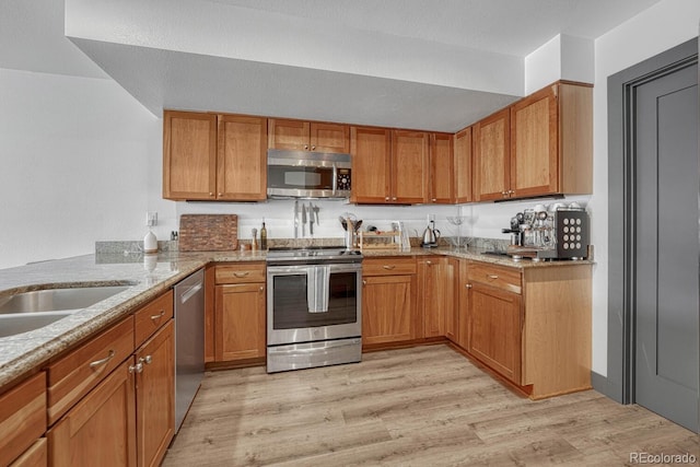 kitchen with brown cabinetry, light stone counters, light wood-style floors, and stainless steel appliances