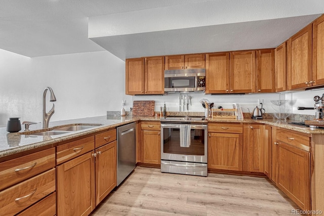 kitchen with brown cabinets, light stone countertops, stainless steel appliances, and a sink