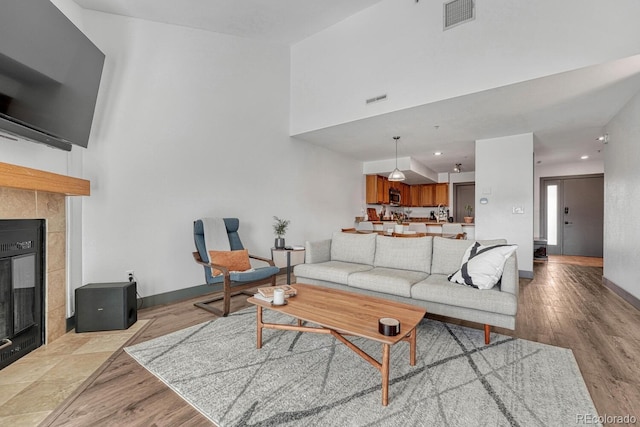 living room with baseboards, light wood-style floors, visible vents, and a tile fireplace
