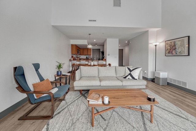living room featuring visible vents, baseboards, a high ceiling, and light wood finished floors