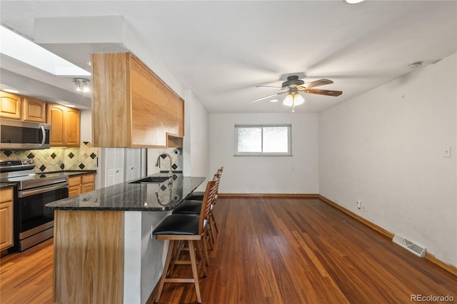 6077 Flower St, Arvada, CO 80004 - kitchen with appliances with stainless steel finishes, a kitchen breakfast bar, backsplash, dark stone counters, and dark wood-style floors