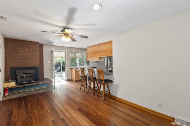 6077 Flower St, Arvada, CO 80004 - kitchen with a ceiling fan, a wood stove, wood finished floors, and a kitchen bar